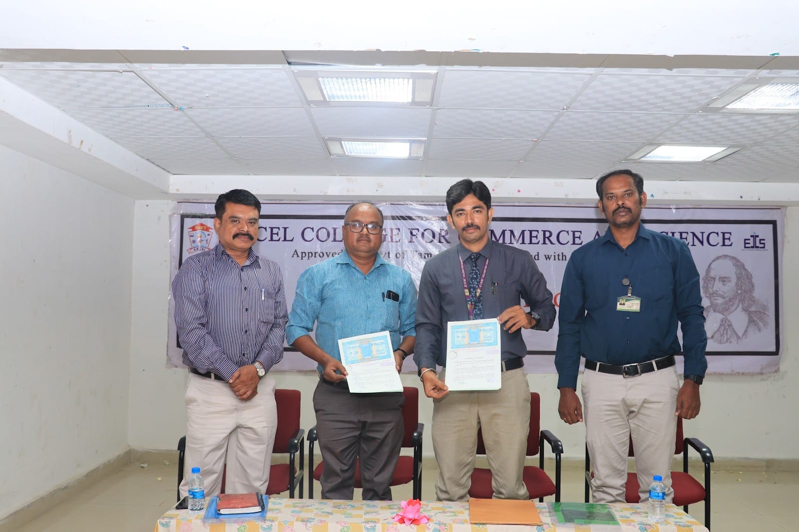 Four men at a college event, two of them holding certificates